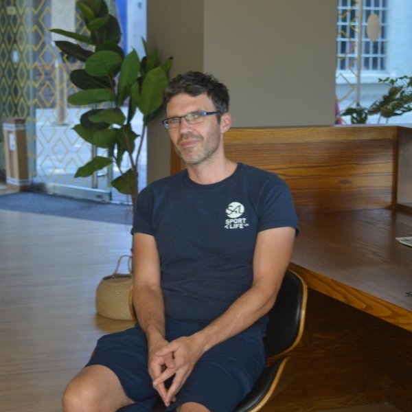White male, dark hair, wearing glasses, sat down on a chair in a Sport 4 Life uniform.