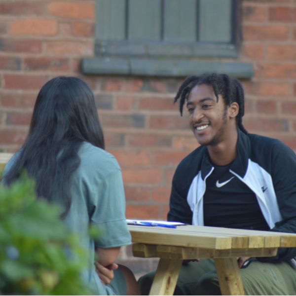 young man on practice interview wearing sports gear sitting opposite woman with black hair on a wooden bench