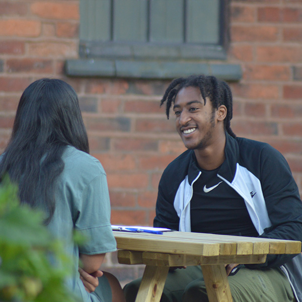 young man on practice interview with sport 4 life wearing sports gear sitting opposite woman with black hair on a wooden bench
