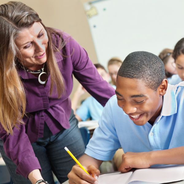 teacher leaning over young boy in secondary school to support him in careers lesson